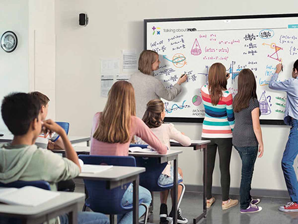 Children in the classroom writing on the whiteboard with a paging speaker on the wall