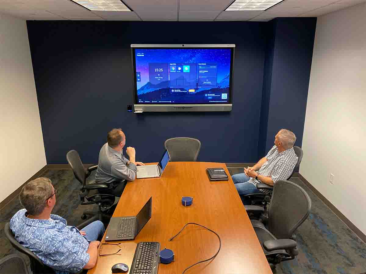 Three men in an EasyRoom conference room looking at a display hanging on a wall