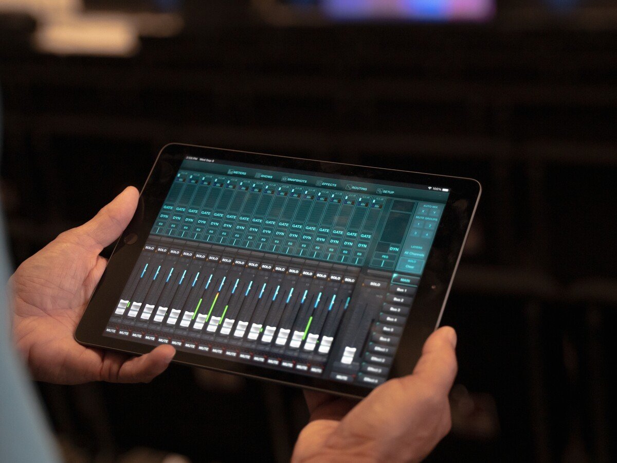 Hands holding an iPad showing a digital audio mixer