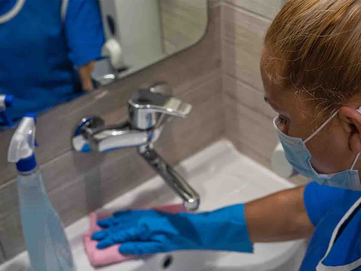Woman in cleaning PPE wiping a sink