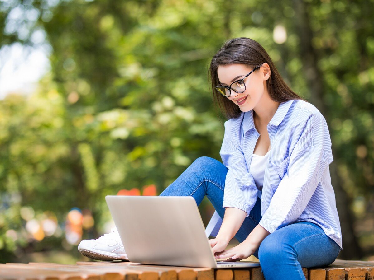 Woman sitting on brick wall using a laptop outside