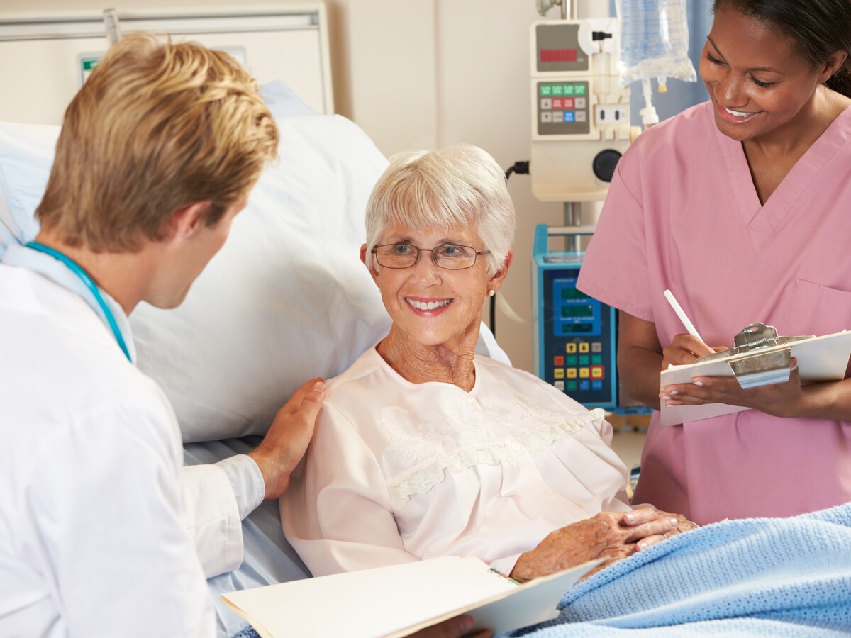 Doctor talking to patient in hospital bed with Nurse taking notes