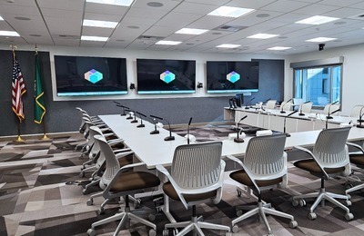A government/public sector conference room with three displays facing a horseshoe shaped conference table with microphones