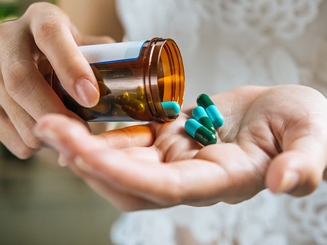 Closeup of hands pouring green pills from a bottle